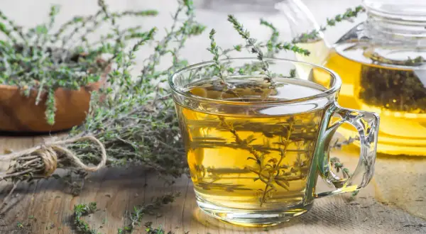Une tasse de tisane de thym le soir, avec une théière en arrière-plan et des brins de thym frais.