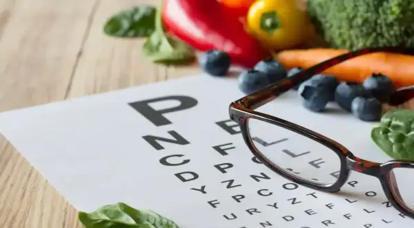 Lunettes sur un tableau d'optométrie entouré de fruits et légumes. La lutéine, présente dans ces aliments, est bénéfique pour la vision.