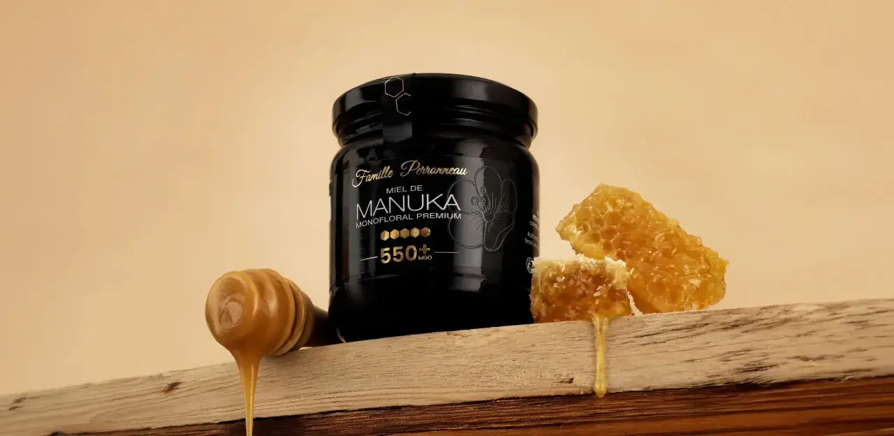 Un pot de miel de Manuka 550+ MGO, avec des rayons de miel et une cuillère à miel dégoulinante. Ce miel de manuka dangereux pour les bactéries, est un trésor de la nature.