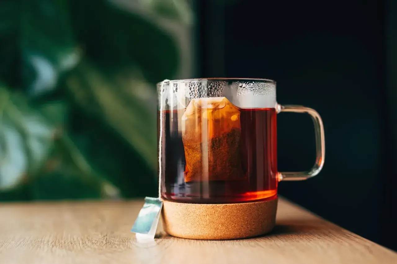 Un moment de détente pour boire du thé après le repas. Une tasse en verre avec un sachet de thé infusant, posée sur un dessous de verre en liège.