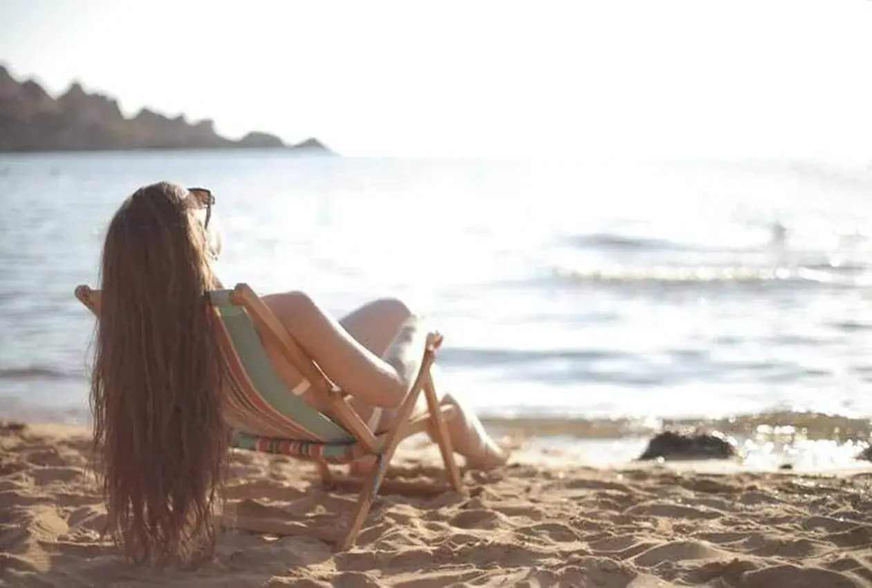 Femme profitant du soleil sur la plage, assise dans une chaise longue, pour faire le plein de vitamine D.