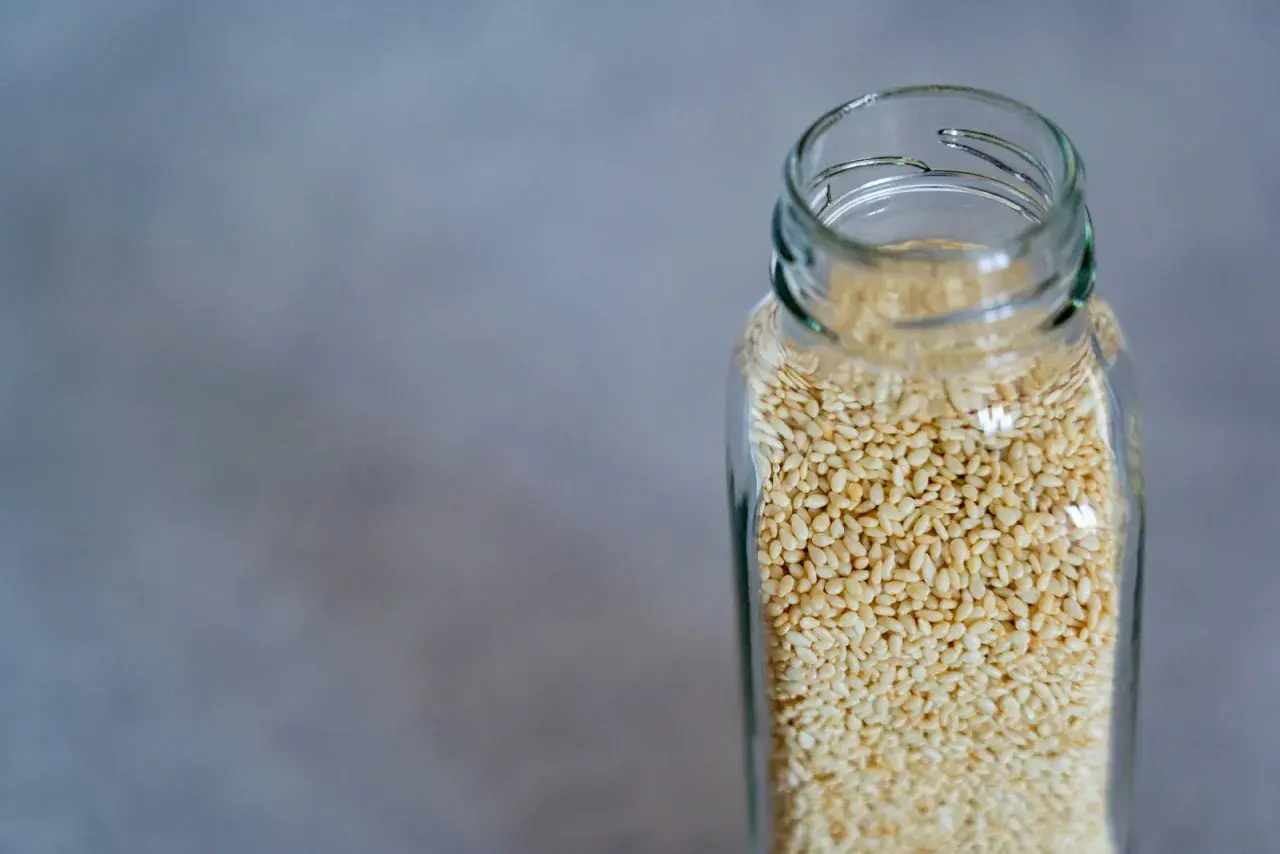 Bain de bouche huile de sésame : un bocal en verre rempli de graines de sésame claires sur fond gris.