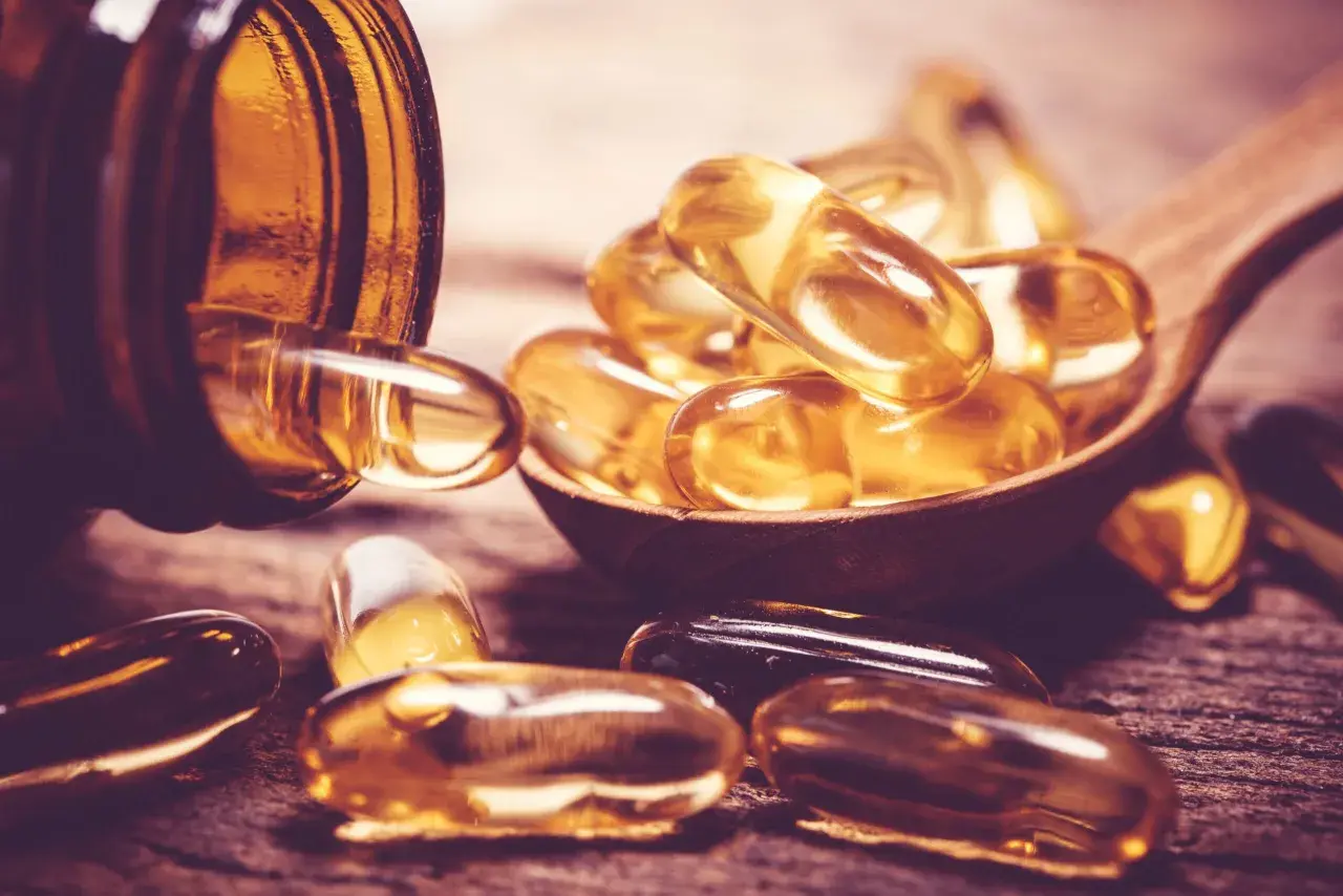 Gélules dorées sur une cuillère en bois, évoquant la vitamine D sans soleil.