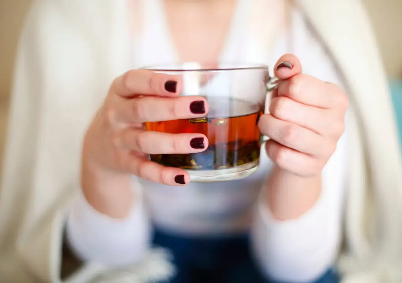 Mains tenant une tasse de thé ambré, se demandant si l'on peut boire des tisanes tous les jours pour un bien-être constant.