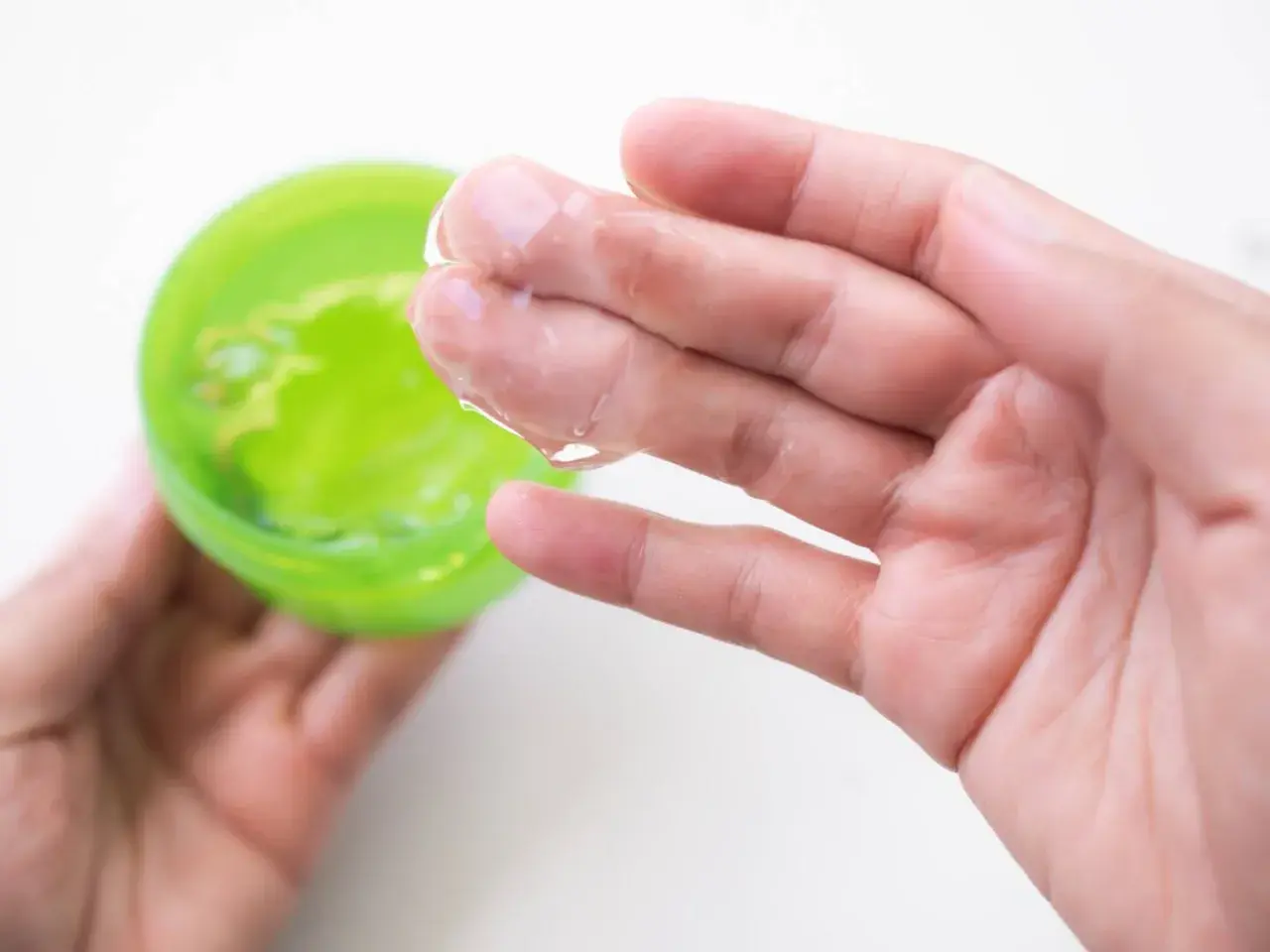 Main tenant une main, une autre prélève un gel transparent d'un pot vert. Attention à l'allergie à l'aloe vera.