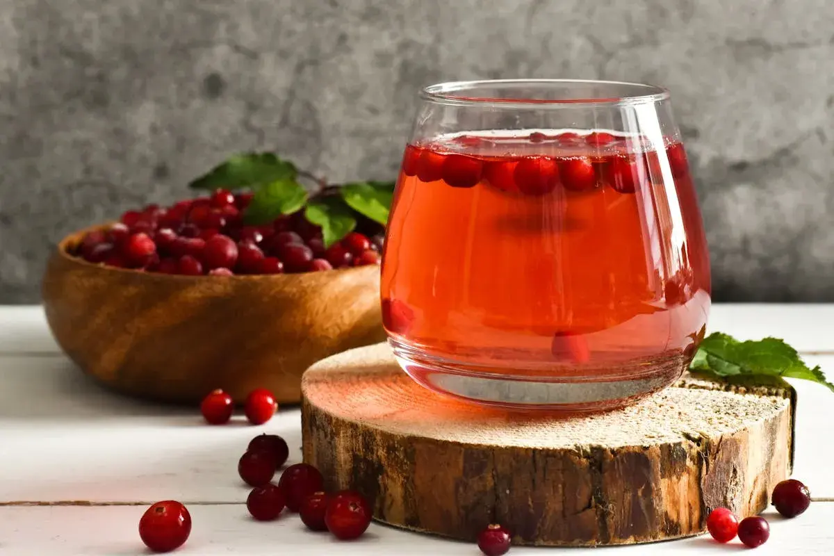 Verre de jus de cranberries, fruit réputé pour aider à prévenir les infections urinaires. Baies rouges dans un bol en bois.