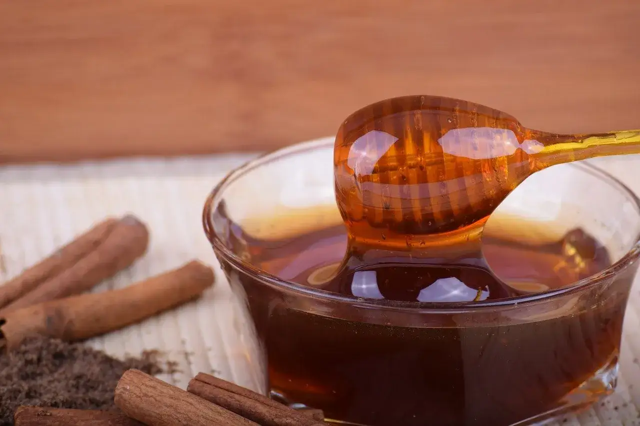 Un pot de miel ambr&eacute; avec une cuill&egrave;re en bois d&eacute;goulinant, entour&eacute; de b&acirc;tons de cannelle. Un d&eacute;lice pour les sens.