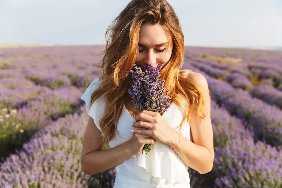 Une femme aux cheveux roux respire un bouquet de lavande dans un champ de lavande. Les lavande bienfaits sont nombreux, comme la relaxation.