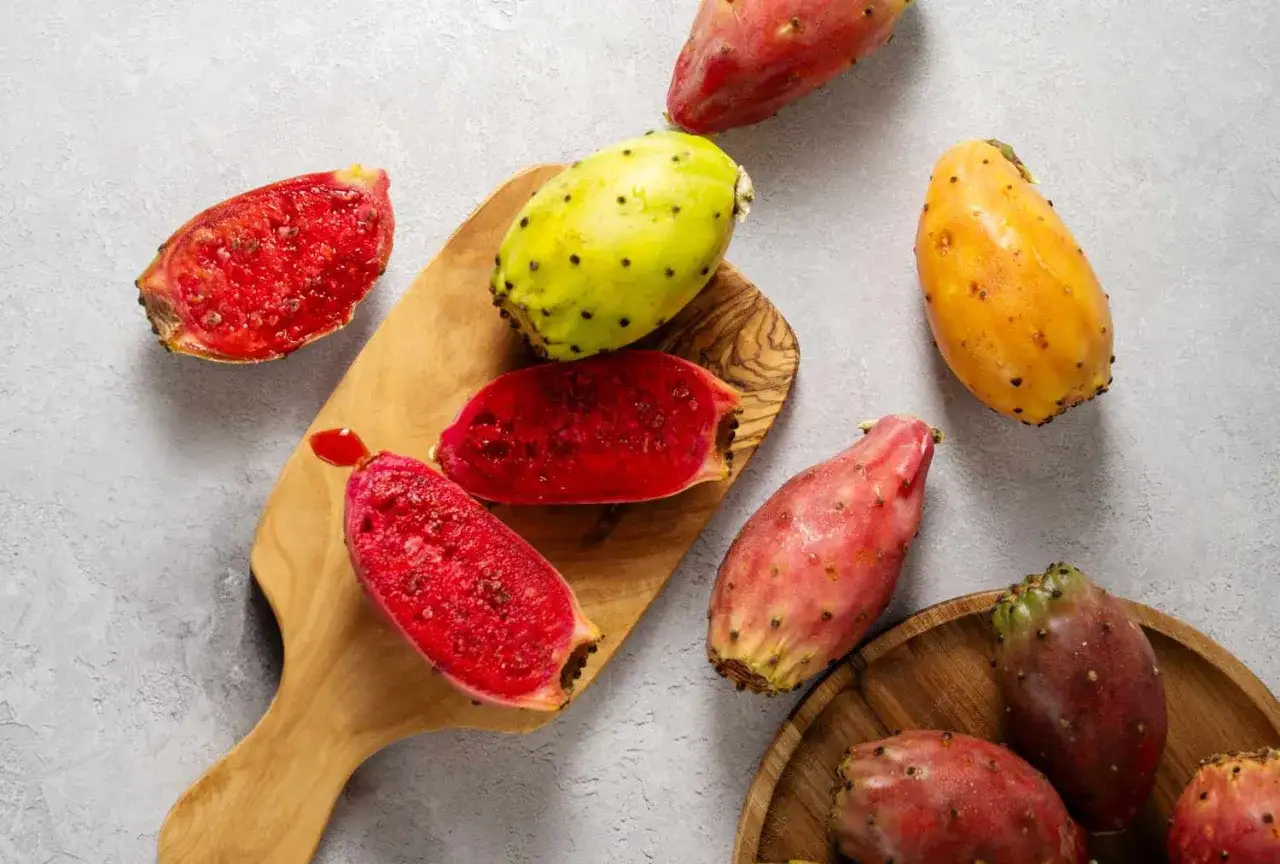 Des fruits de le nopal, certains entiers aux couleurs vives (rose, jaune, orange), d'autres coup&eacute;s r&eacute;v&eacute;lant une chair rouge juteuse et piquante.