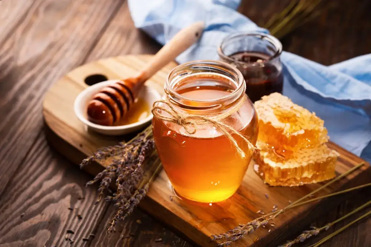 Un pot de miel ambré, des rayons de miel et de la lavande sur fond de bois. Découvrir les propriétés du miel.