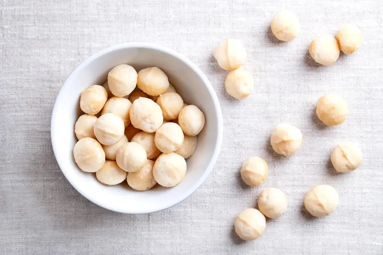 Un bol de noix de macadamia, connues pour leurs nombreux noix de macadamia bienfaits, est posé sur un tissu texturé.