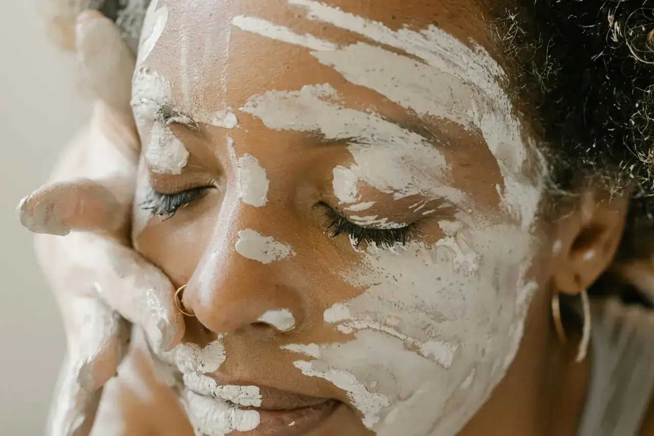 Une femme applique un masque d'argile verte sur son visage, espérant soulager son eczéma. Ses yeux sont fermés, profitant de ce moment de soin.