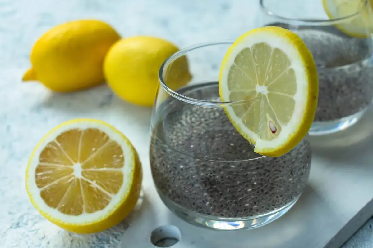 Verre de graine de chia dans l'eau, garni d'une tranche de citron. Des citrons entiers et une moitié de citron sont disposés à côté.
