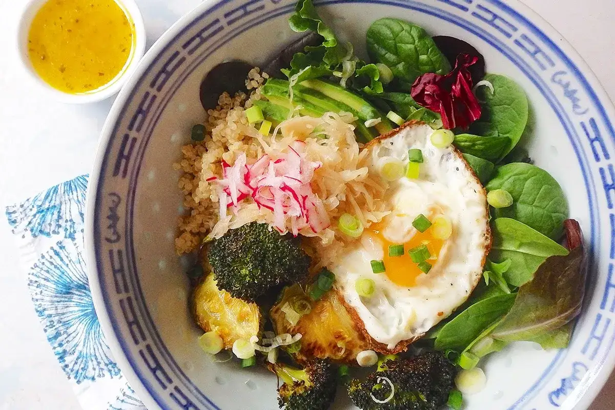 Bol avec quinoa, œuf au plat, brocolis rôtis, avocat, choucroute et radis. Un repas sain, plein d'aliments bons pour l'estomac et les intestins.