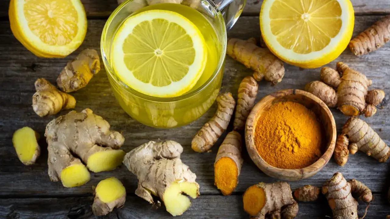 Infusion de citron et de gingembre anti inflammatoire, entour&eacute;e de racines de gingembre frais et de curcuma en poudre.