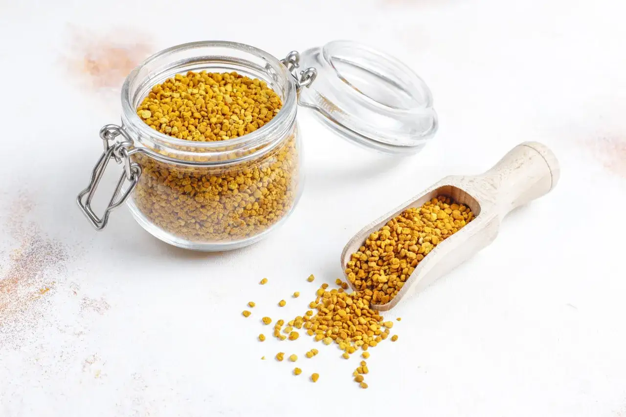 Un pot en verre et une cuillère en bois débordent de pollen d'abeille doré.