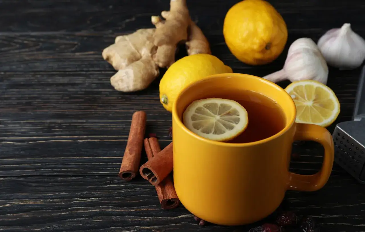 Une tasse de thé jaune avec une tranche de citron, du gingembre, des citrons, de l'ail et de la cannelle. Un remède de grand-mère contre le rhume de cerveau.