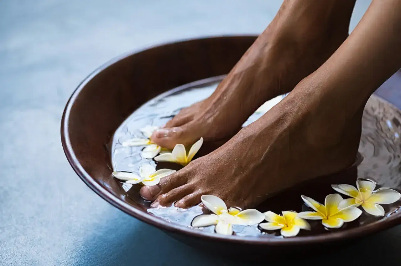 Pieds dans un bain de pied relaxant avec des fleurs de frangipanier. Un moment de d&eacute;tente avec du sel d'Epsom pour un soin des pieds parfait.