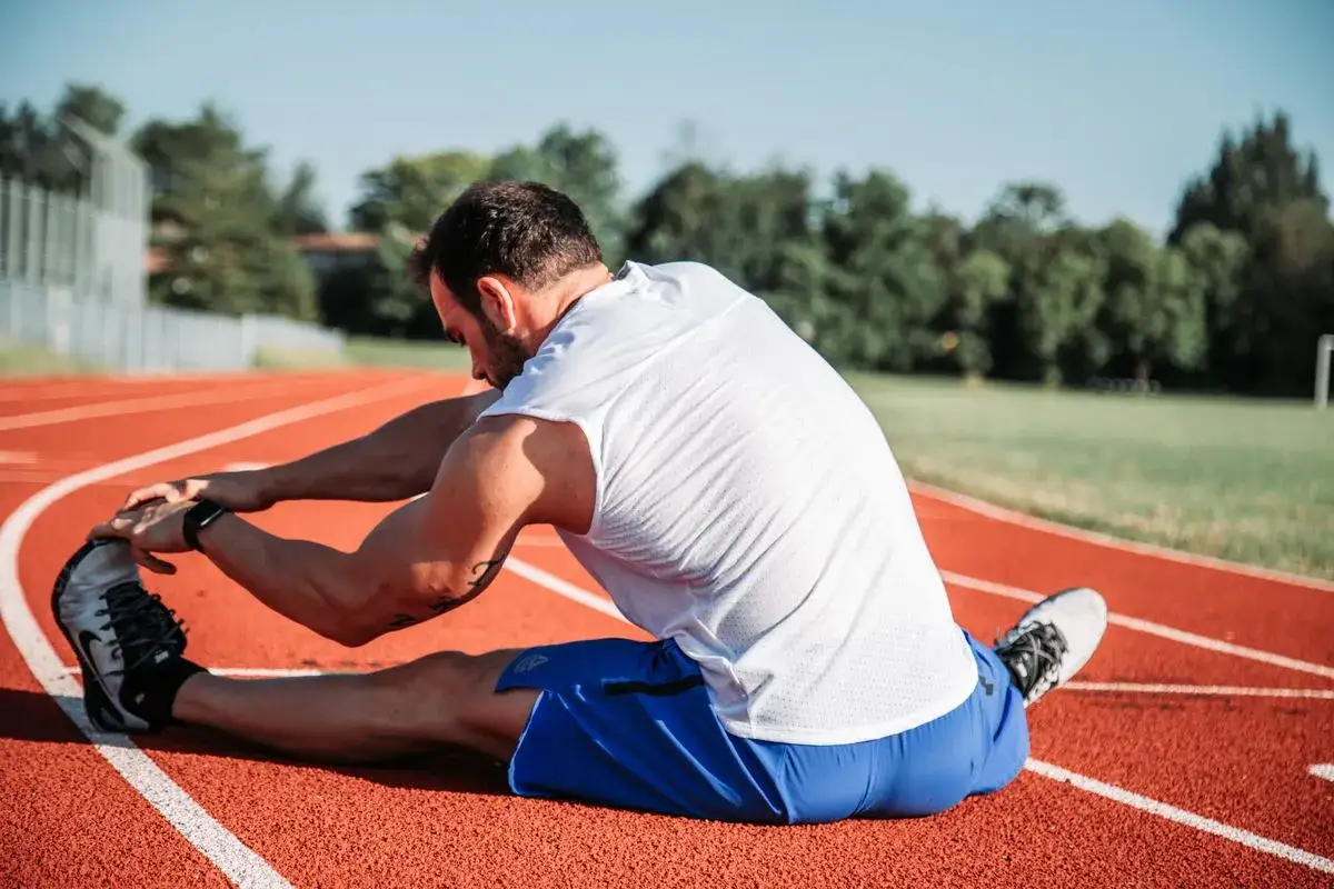 Un athlète s'étire sur une piste, une routine essentielle pour comment éviter les crampes pendant l'effort.