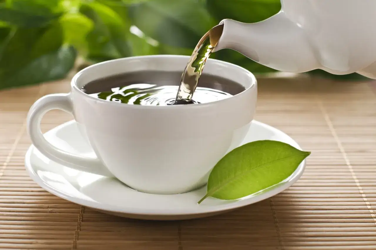 Th&eacute; vert vers&eacute; dans une tasse blanche, avec une feuille pos&eacute;e sur la soucoupe. Id&eacute;al pour conna&icirc;tre la dose maximale de th&eacute; vert par jour.