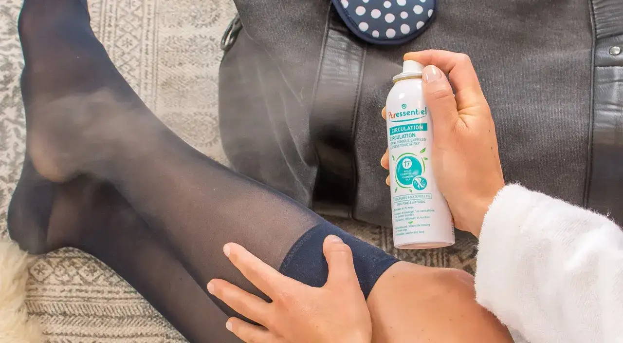 Jambes fatiguées soulagées par un spray tonique. Une main applique le produit sur une jambe portant un bas bleu marine.