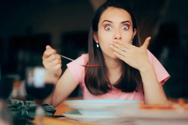 Femme surprise avec une cuillère de soupe, main sur la bouche, comme si elle avait le hoquet persistant.