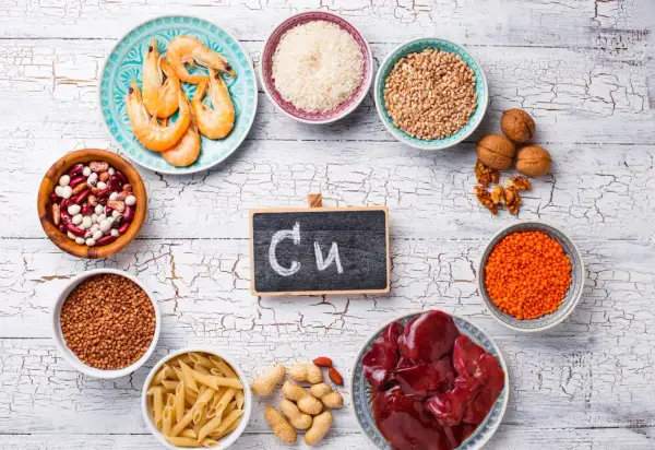 Assiette de crevettes, bols de riz, lentilles, haricots, pâtes, cacahuètes, noix, foie et un tableau noir avec "Cu" pour les cuivre bienfaits.