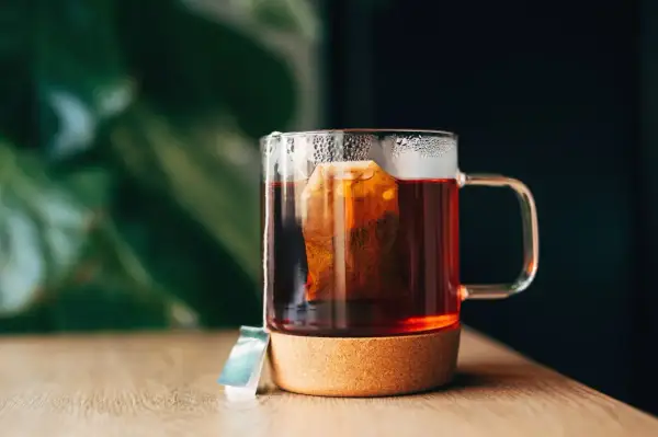 Un moment de détente pour boire du thé après le repas. Une tasse en verre avec un sachet de thé infusant, posée sur un dessous de verre en liège.