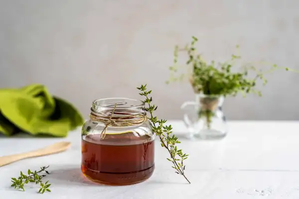 Un bocal de miel ambré, orné de brins de thym frais, évoque les bienfaits naturels de ce trésor doré.