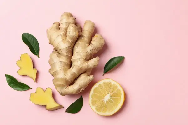 Gingembre anti inflammatoire, citron et feuilles vertes sur fond rose. Un remède naturel pour le bien-être.