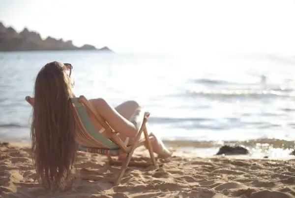 Femme profitant du soleil sur la plage, assise dans une chaise longue, pour faire le plein de vitamine D.