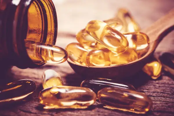 Gélules dorées sur une cuillère en bois, évoquant la vitamine D sans soleil.