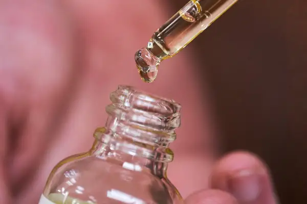 Une goutte d'huile de ricin tombe d'une pipette dans un flacon. Découvrez les bienfaits de l'huile de ricin pour vos cheveux et votre peau.