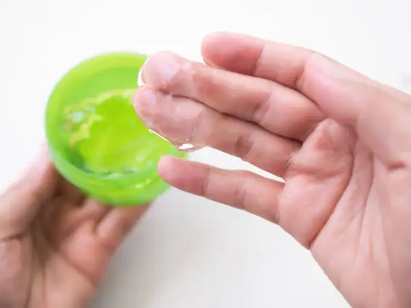 Main tenant une main, une autre prélève un gel transparent d'un pot vert. Attention à l'allergie à l'aloe vera.