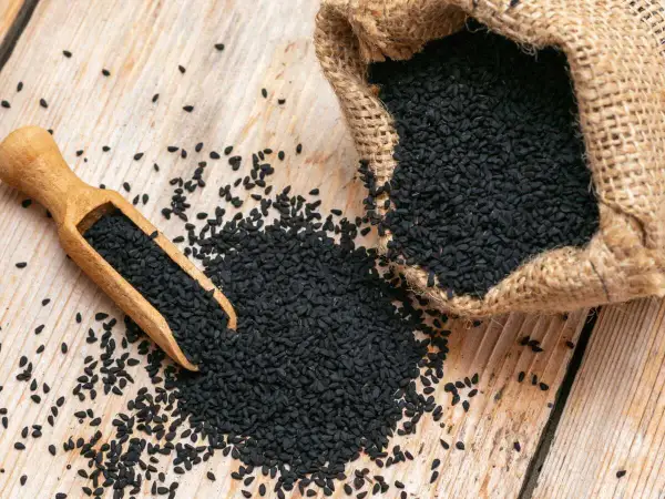 Graine de nigelle : découvrez les nombreuses vertus de ces petites graines noires, ici présentées dans une cuillère en bois et un sac en toile de jute.