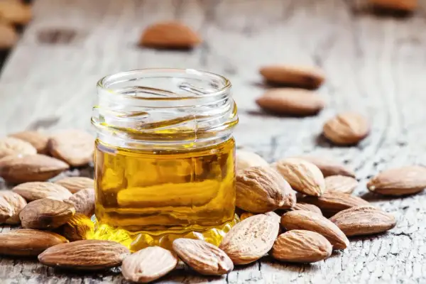 Un petit pot d'huile d'amande douce, entouré d'amandes entières sur fond de bois. Découvrez les bienfaits de l'huile d'amande douce pour la peau.