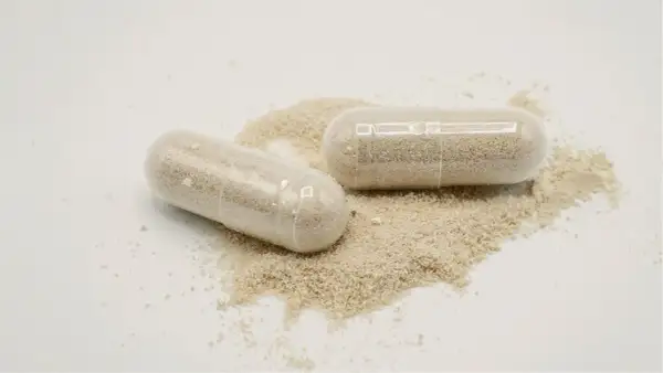 Deux gélules transparentes remplies de poudre beige, posées sur un tas de poudre. Une dose maximale de vitamine D pour votre bien-être.