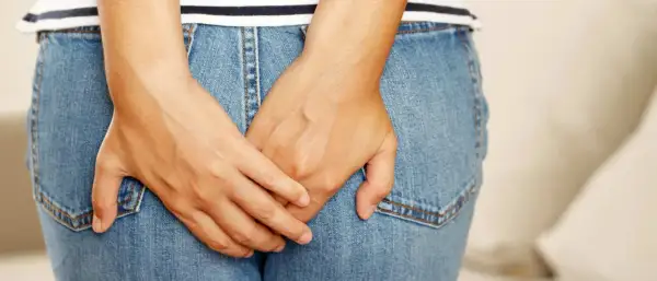 Mains croisées sur un jean, suggérant un inconfort. Apprenez comment se débarrasser des vers intestinaux naturellement.