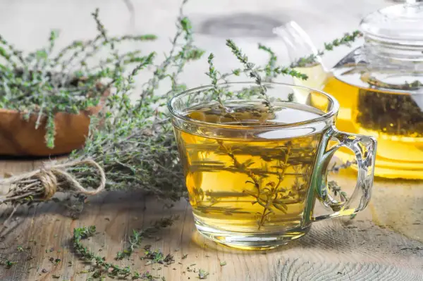 Une tasse de tisane de thym le soir, avec une théière en arrière-plan et des brins de thym frais.